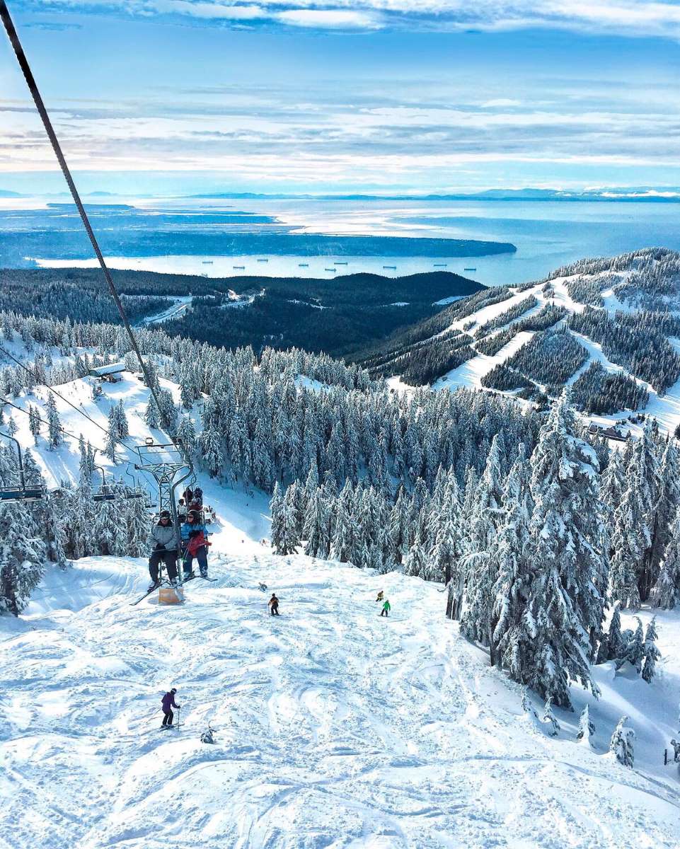 Downhill skiers and snowboarders on Cypress Mountain with views of the chairlift and Vancouver